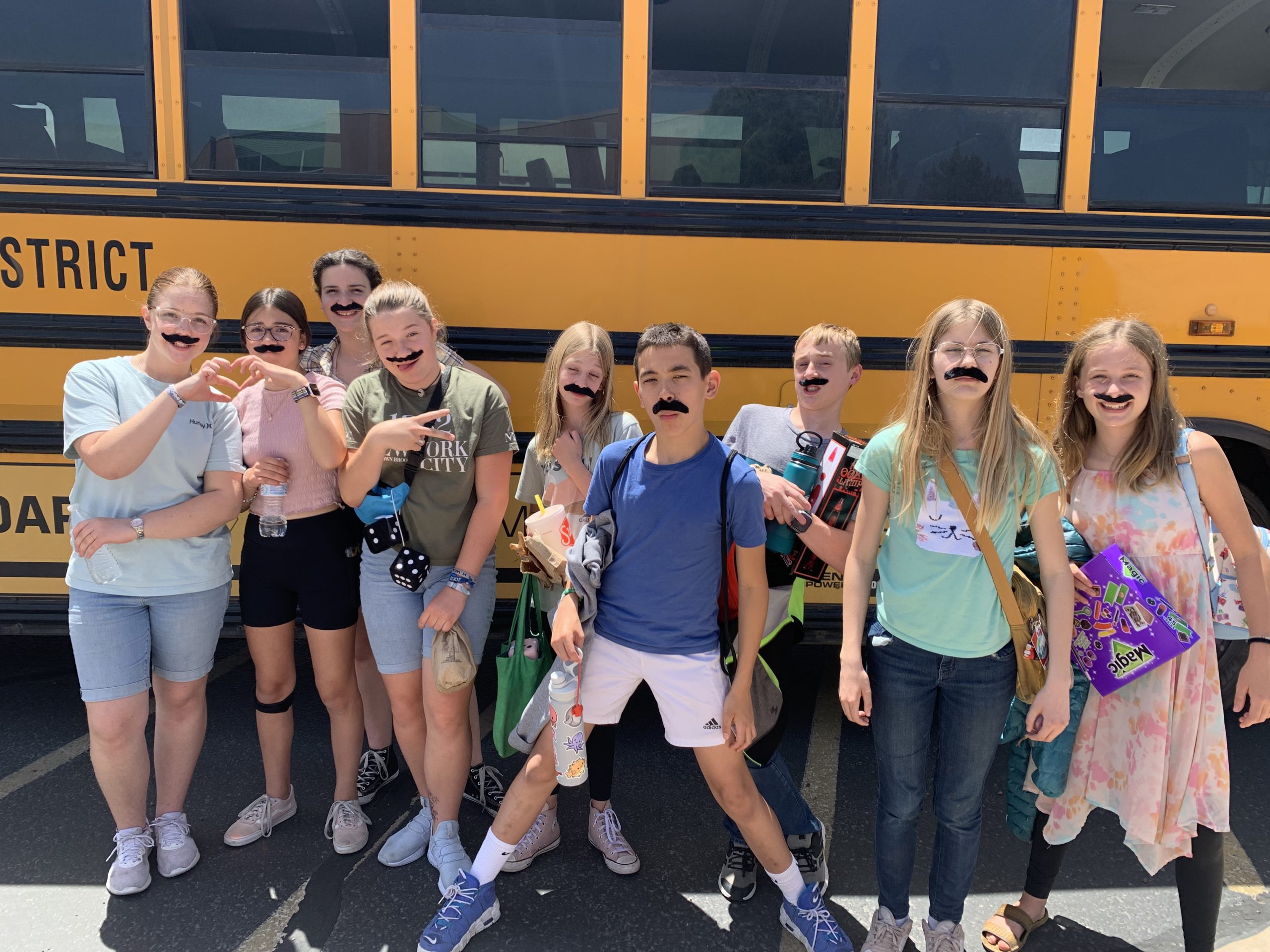 7th graders showing off their mustaches standing in front of the school bus.