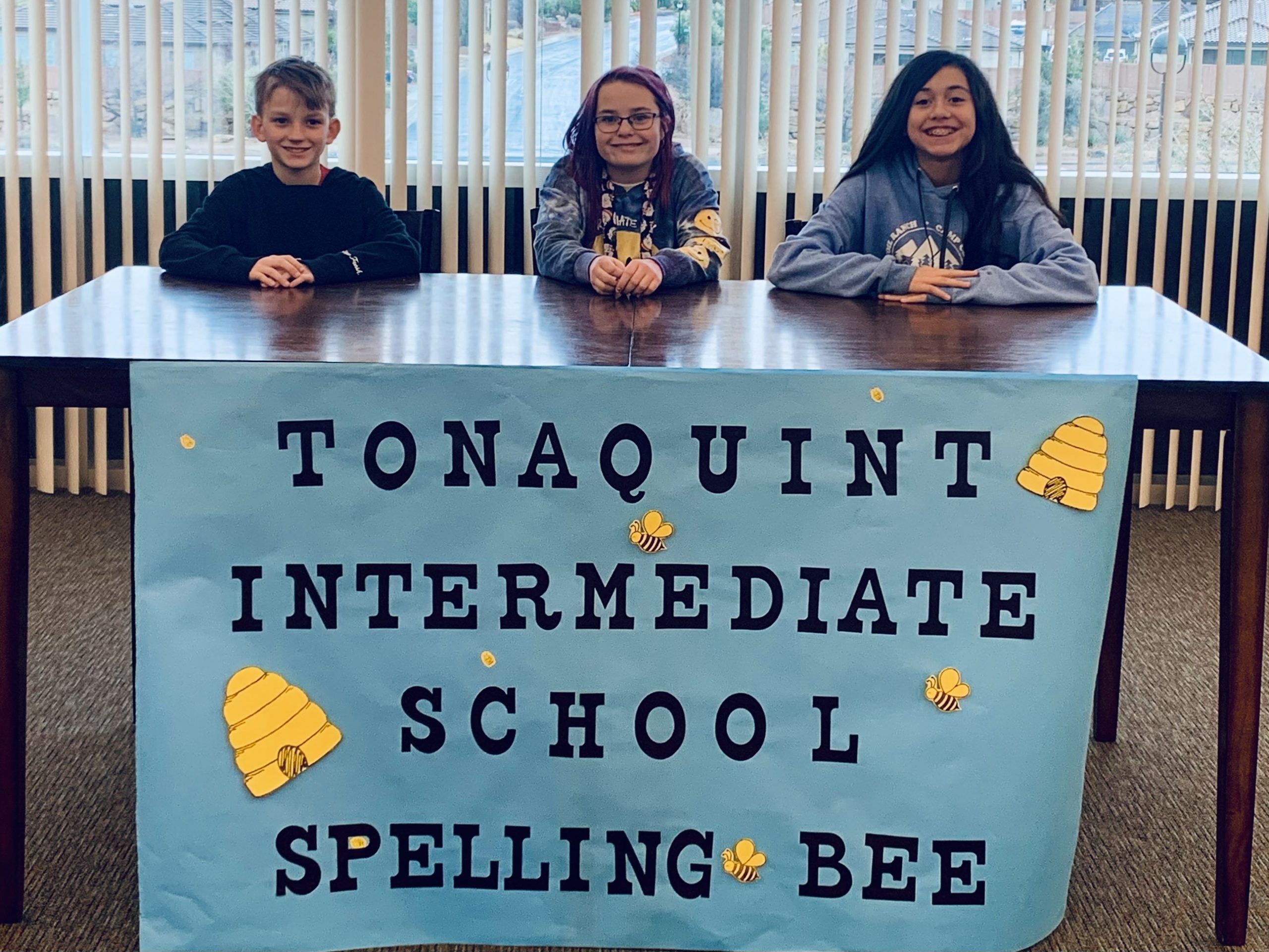 Tonaquint's top three spellers sit at a table with the "Tonaquint Spelling Bee" sign taped to it.