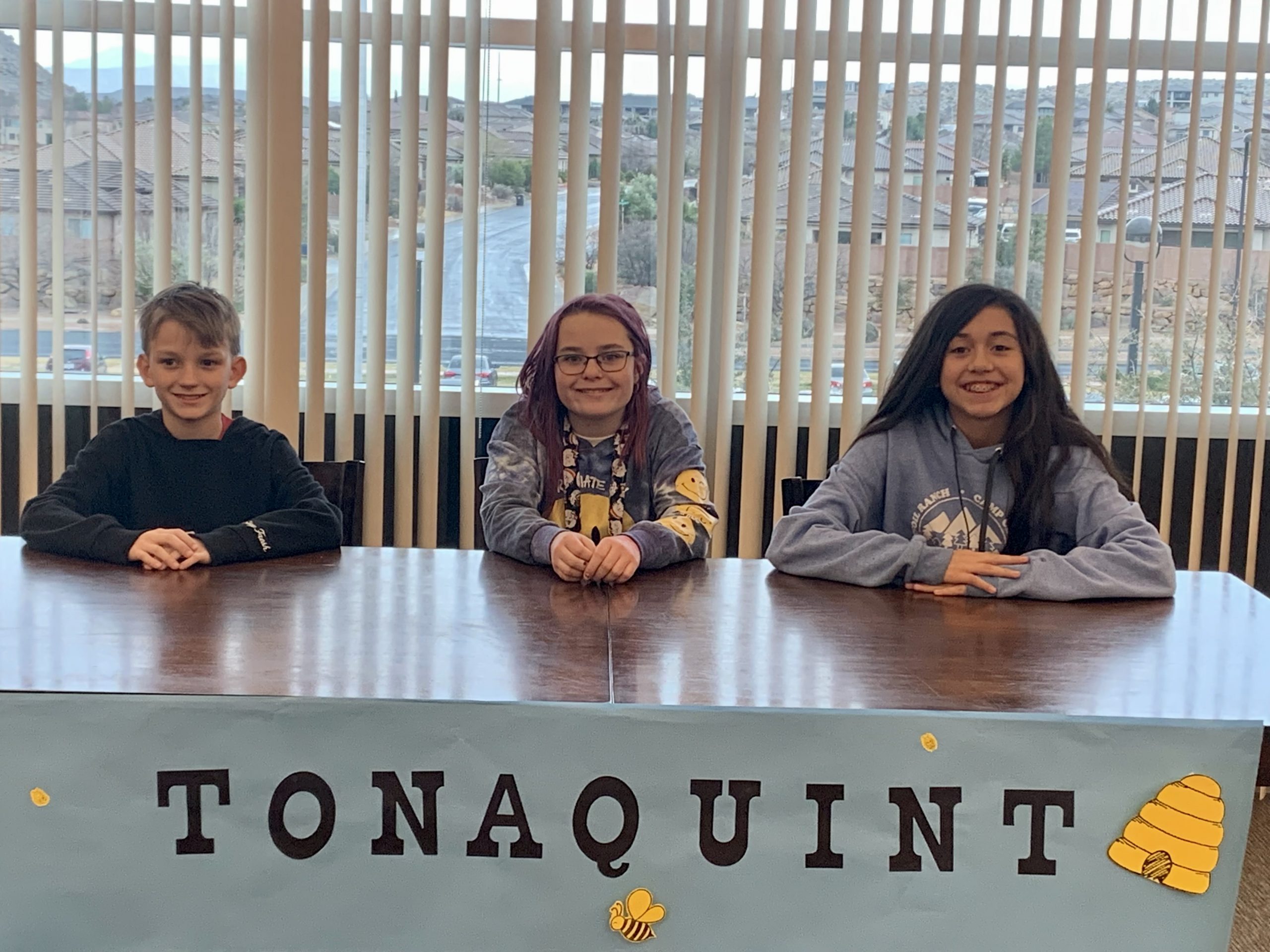 Top three spellers of the Tonaquint Spelling Bee sitting at a table behind the spelling bee sign.