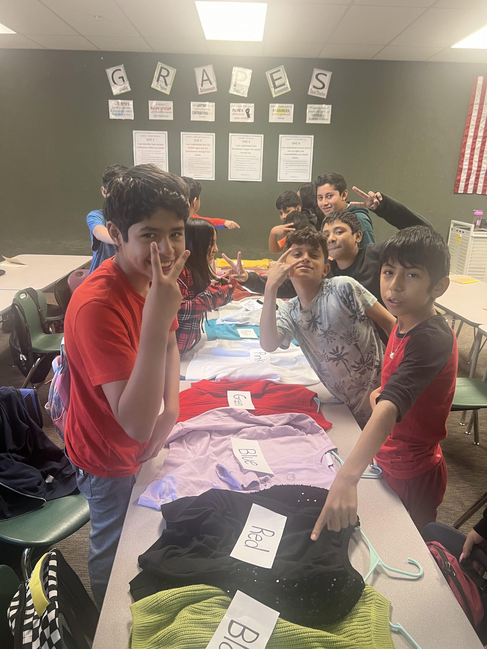 Ms. Bryan's ESL class matches color words (in English) with the corresponding article of clothing laying out on the long table.