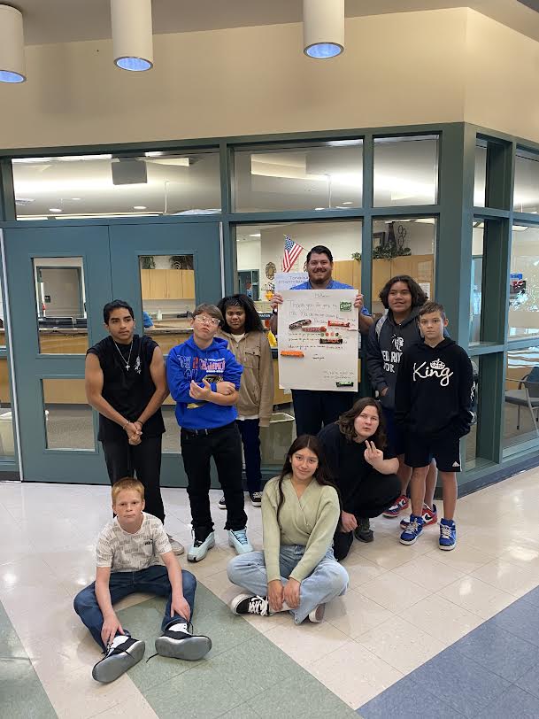 Eight 7th grade Tonaquint students pose in front of the office with Mr. Rarick with the candy bar poster/card that they made for him during principal appreciation week.