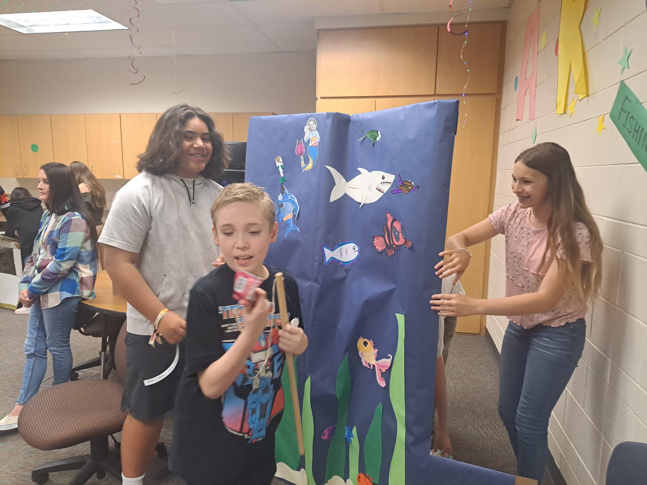 One of Ms. Miller's students examines his prize from the "Go Fish" booth while the students who created the booth look on.