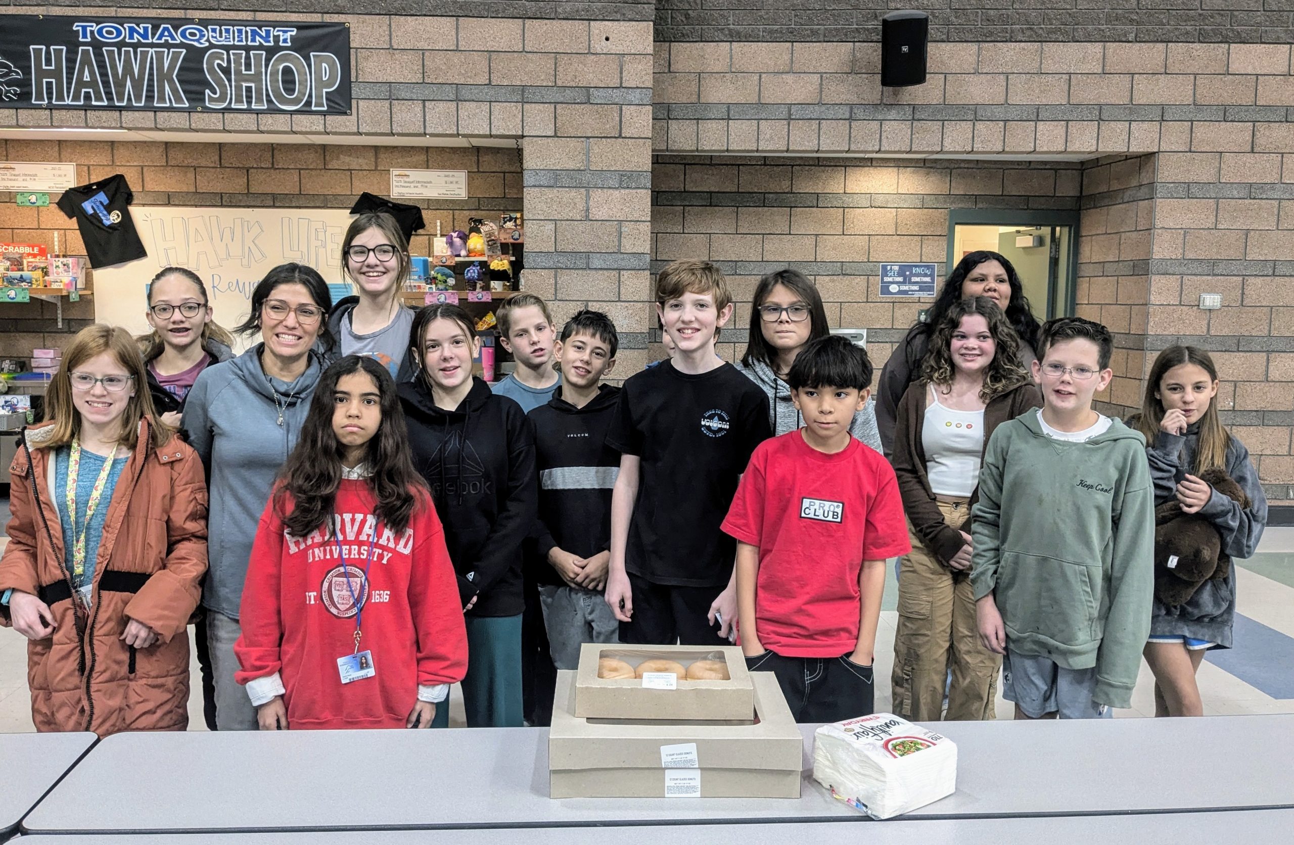 Ms. Jorgensen's homeroom class pose in font of the Hawk Shop with their donut reward for winning the best 7th grade Spirit Week Door Decorating Contest.